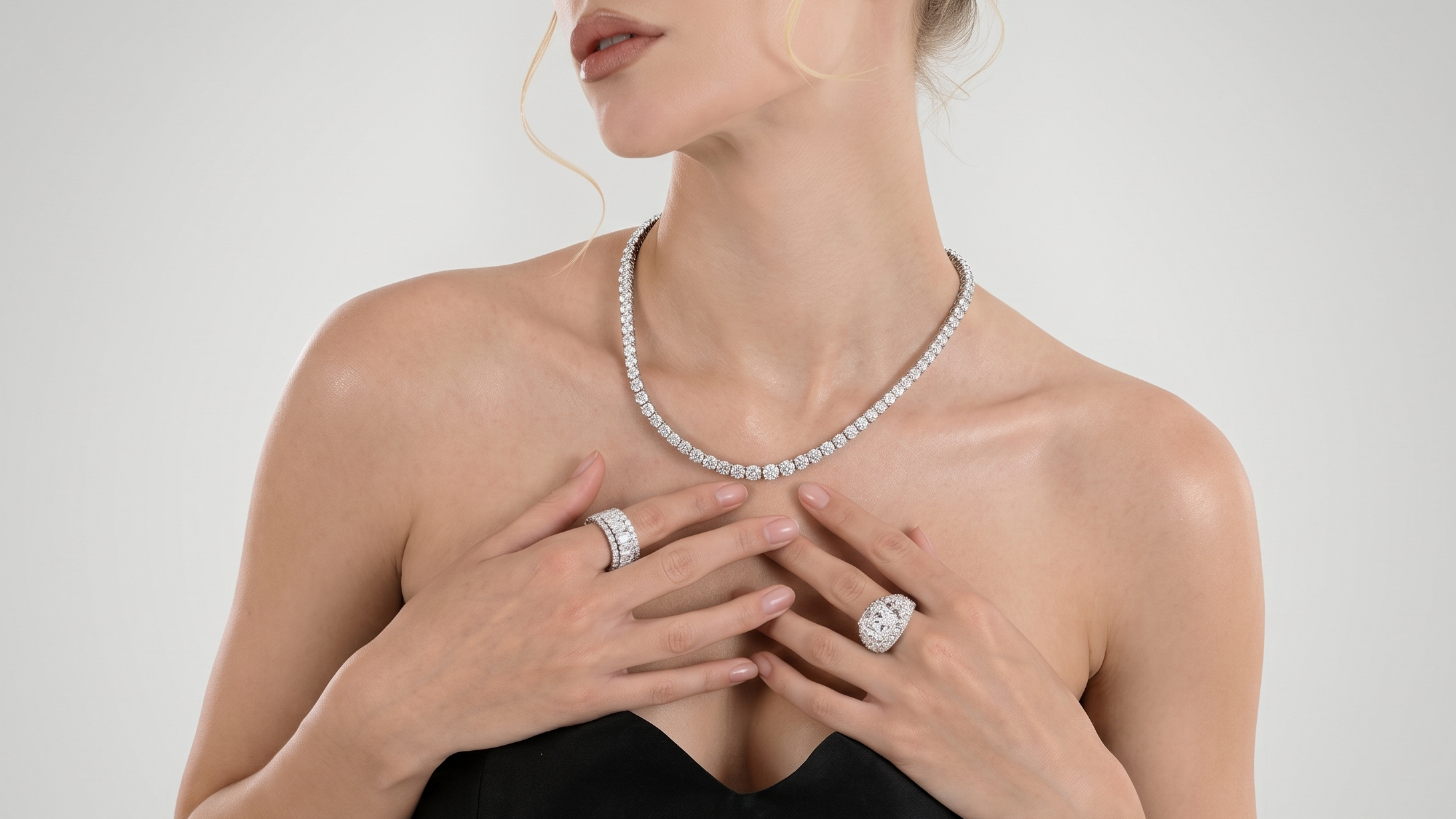 A woman wearing a diamond necklace, matching diamond rings, and a watch with a silver-toned band, posed against a light gray background.
